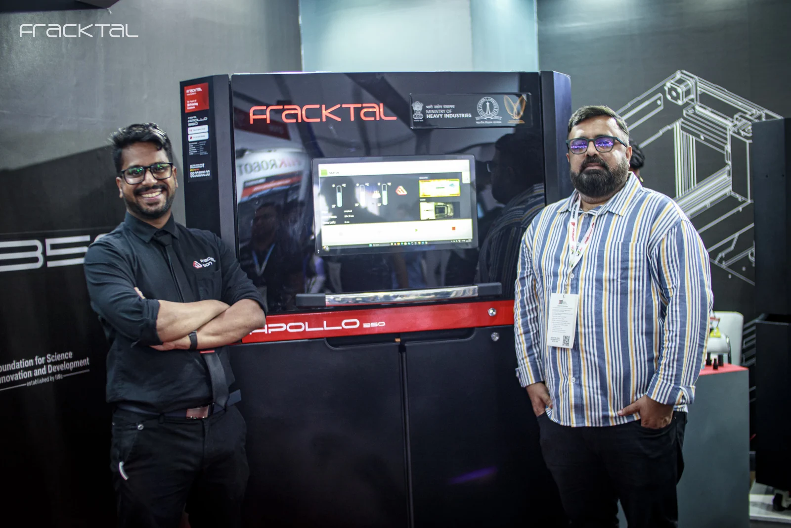 Vijay Raghav Varada beside the Apollo 350 SLS printer on the Fracktal stand at IMTEX, the Ministry of Heavy Industries and FSID-IISc emblems on the backdrop behind him.