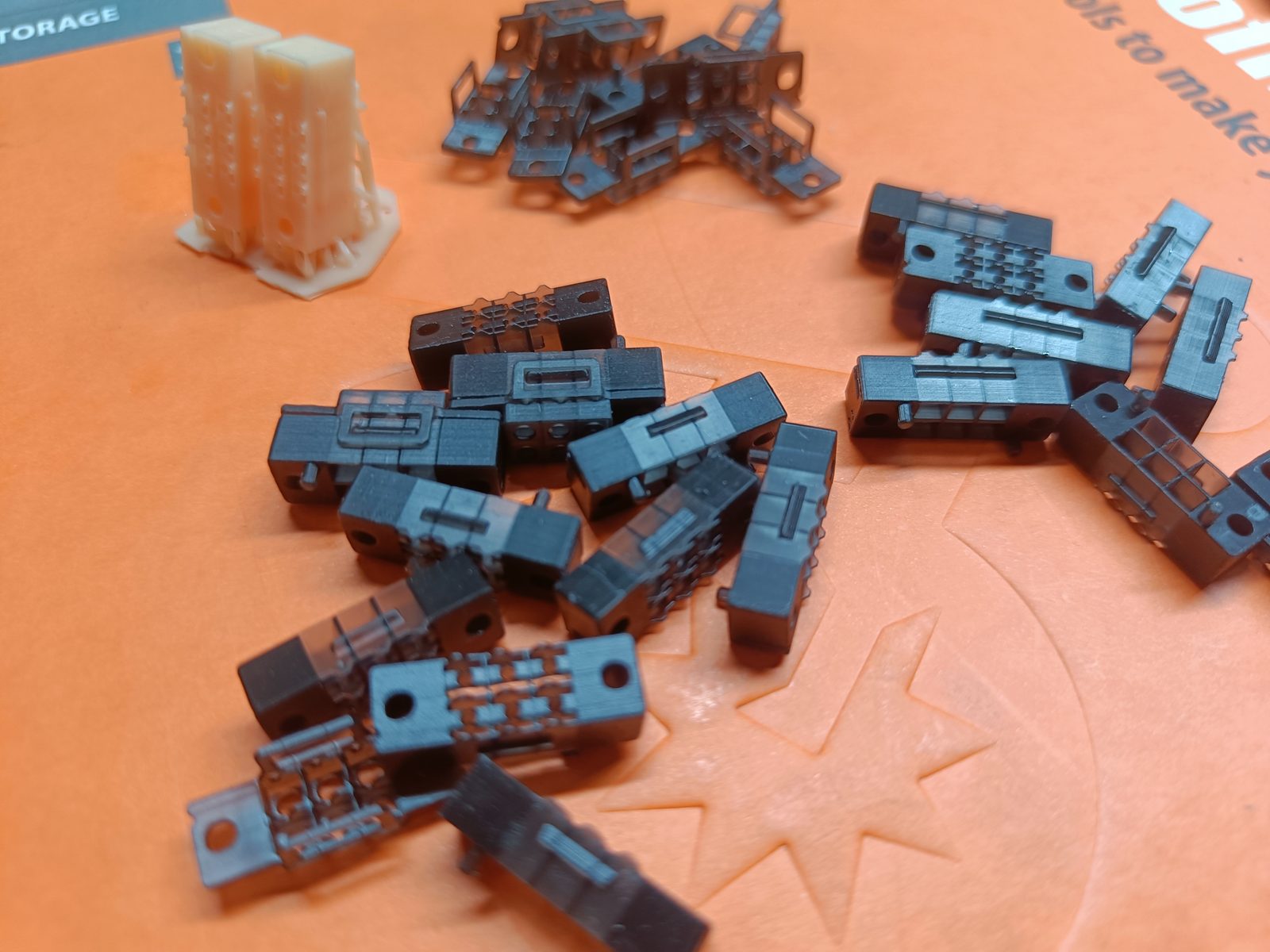 Dozens of small printed Braille mechanism parts scattered on an orange cutting mat.