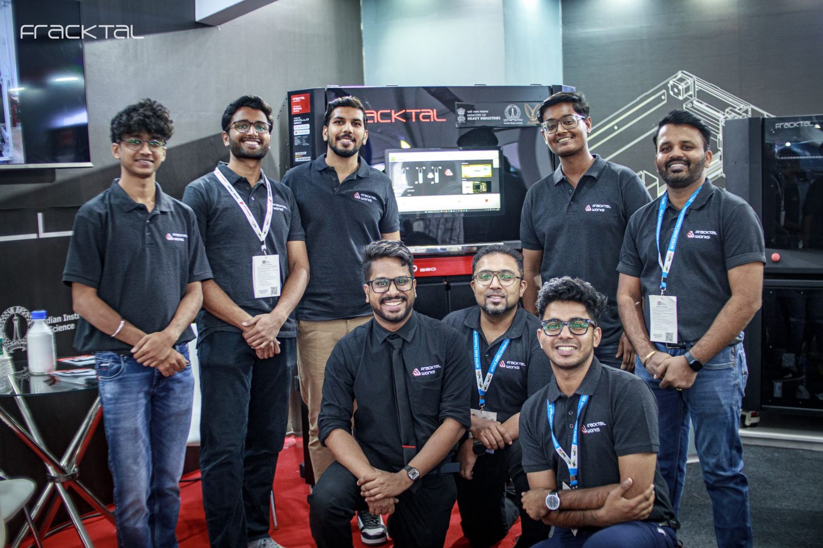 The Fracktal Works team at a trade stand, in front of their machines.