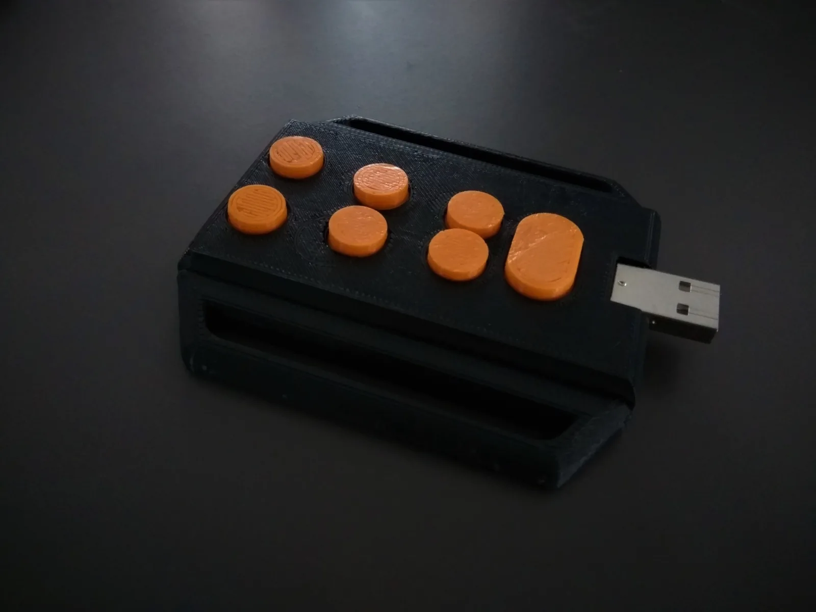 Tipo: a black 3D printed Braille keypad with six orange keys in two columns and a USB plug at one end, on a dark background.