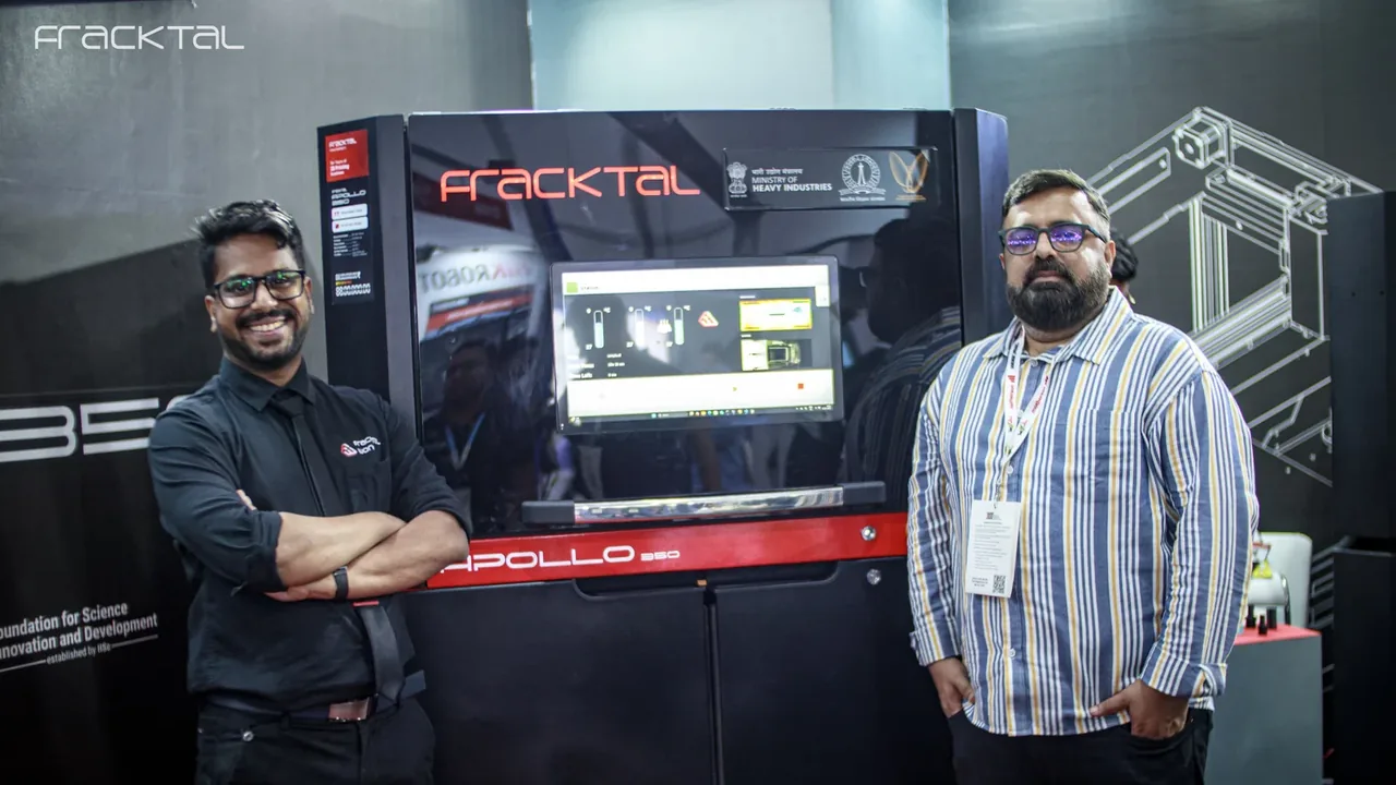 The Apollo 350 SLS printer on the Fracktal stand at IMTEX, with two of the team in front of it.