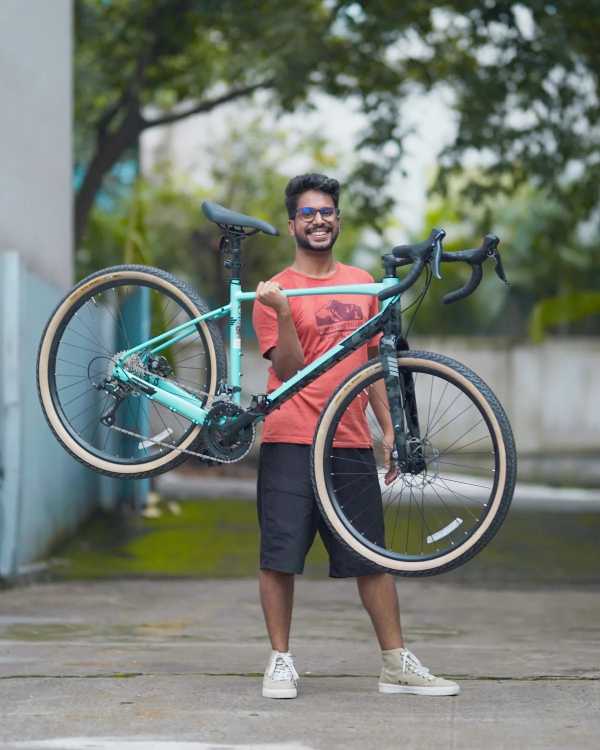 Vijay Raghav Varada, smiling, holding a mint green gravel bicycle up by its frame.