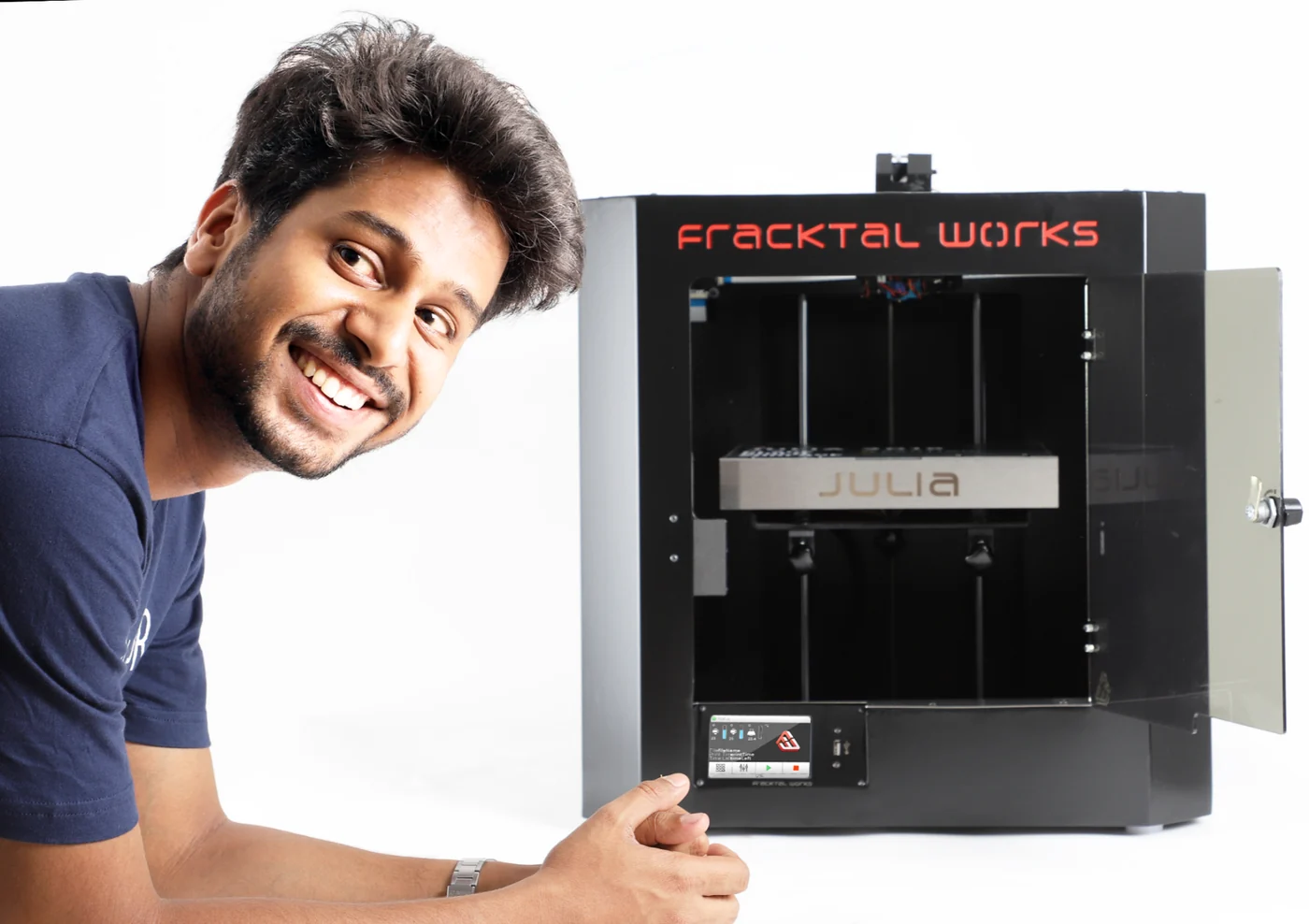 Vijay Raghav Varada leaning into frame beside an open Fracktal Julia 3D printer, smiling.